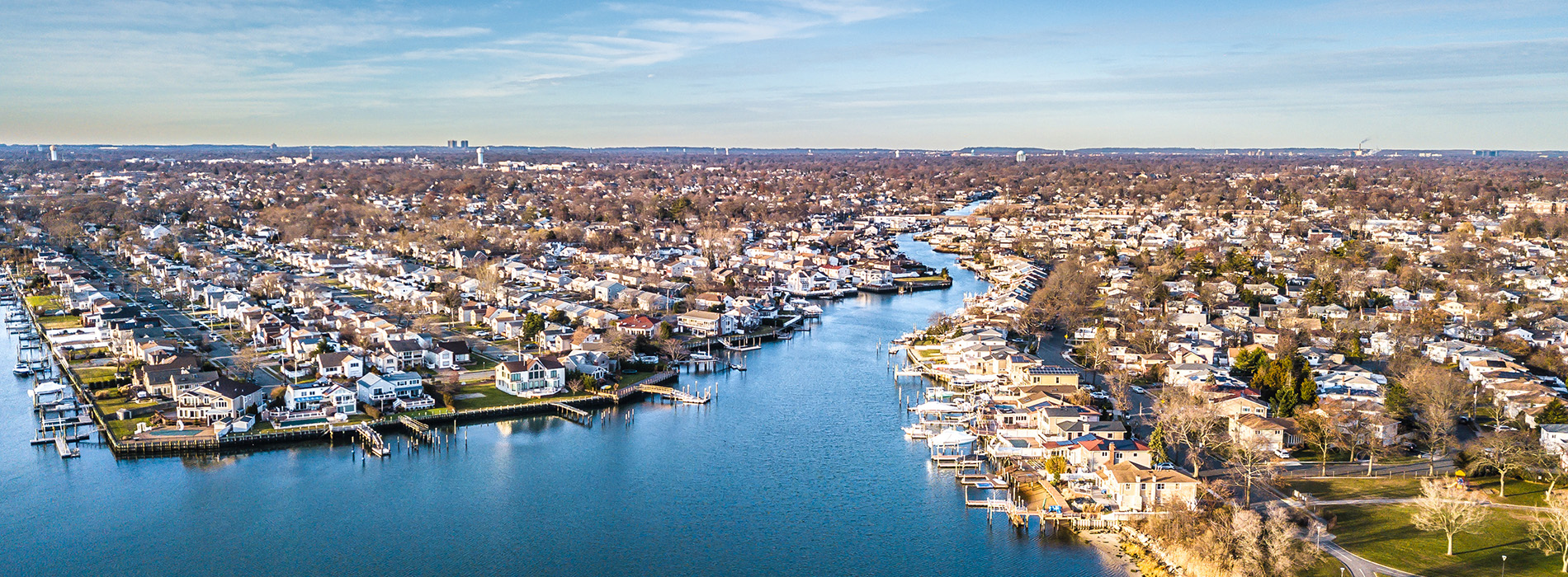 The image shows a panoramic view of a cityscape with a river running through it, featuring multiple houses and boats on the water.