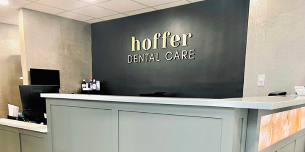 The image shows an interior view of a dental care office named  Hoffer Dental Care.  The space appears modern and clean, with a reception area featuring a counter, signage, and a waiting room.