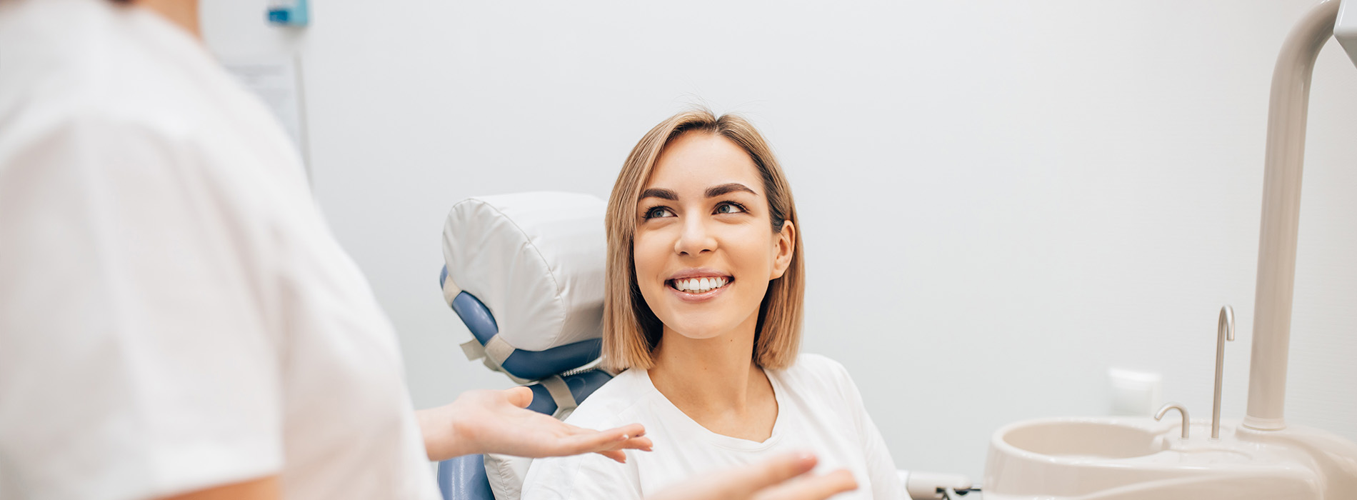 A dental professional in a white coat attending to a patient with a smile, both seated in a dental chair.