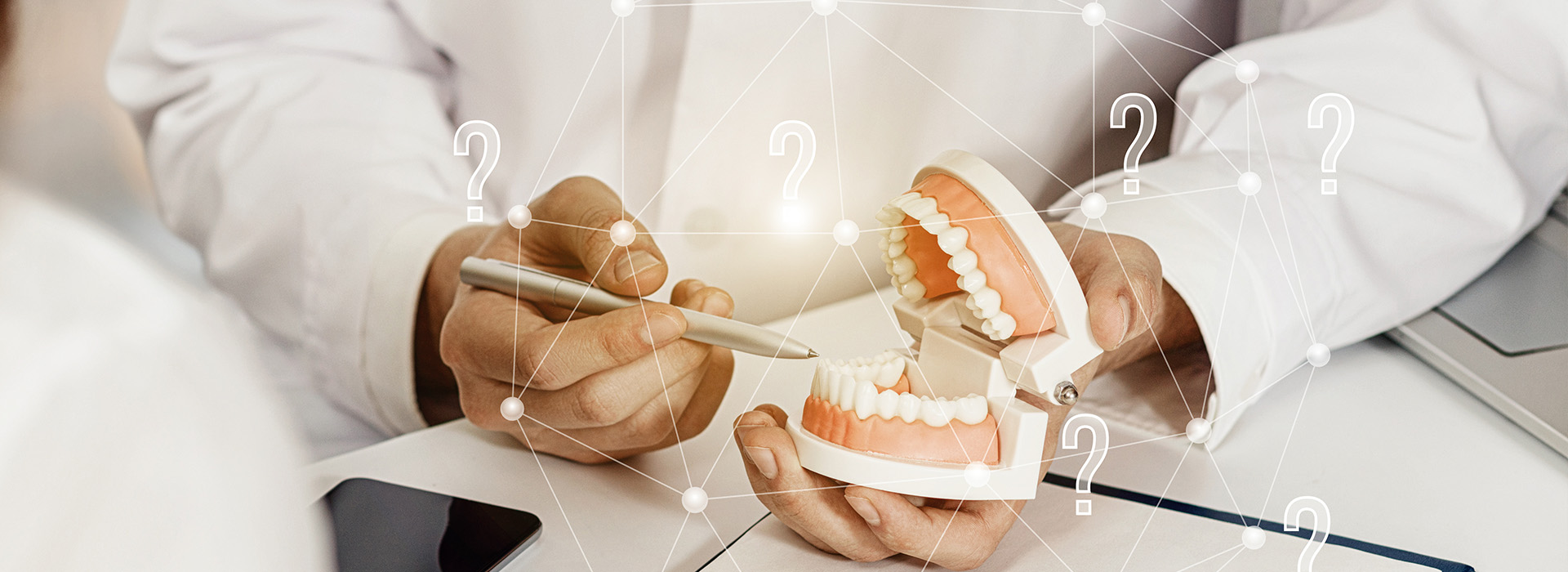 An image of a person s hand holding dental implants in front of an open laptop displaying various numbers and icons, with a blurred background featuring a medical professional.