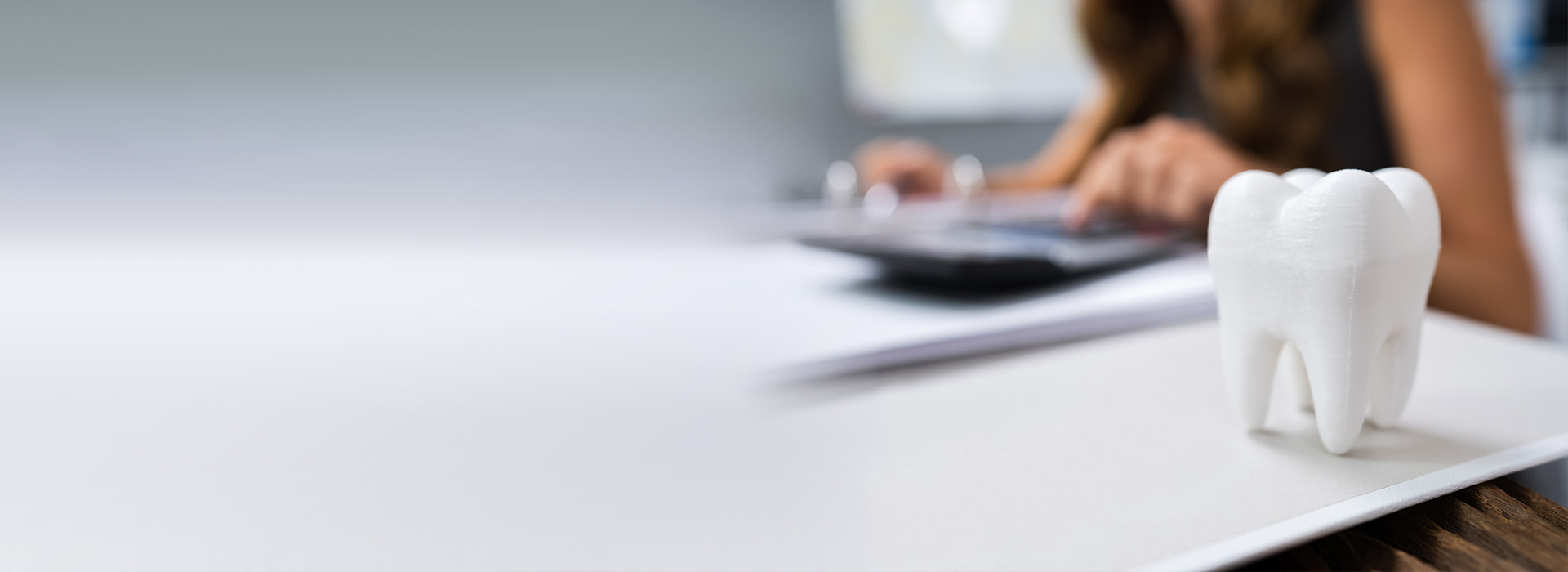 The image shows a person working at a desk with a whiteboard and a small figurine of a person s head on the table, set against an office background.