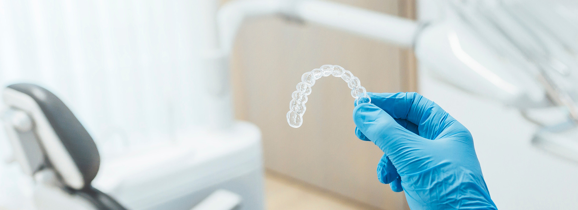 The image shows a hand in a blue glove holding a transparent dental impression material, with the background featuring a dental office setting.