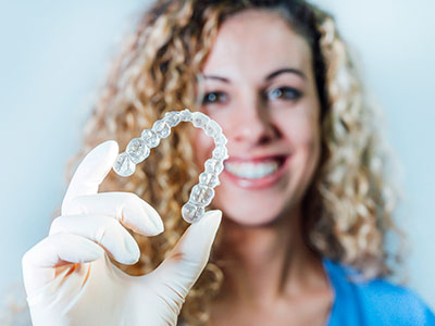 A woman wearing a surgical mask is holding up a clear plastic dental retainer.