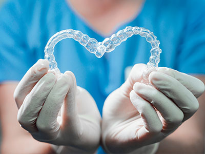 A hand holding a heart-shaped clear dental retainer.