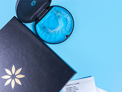 An open box of dental floss with a blue lid and toothpaste tube on a light blue background.