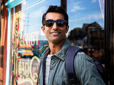 A man wearing sunglasses and a backpack, standing in front of a shop window.