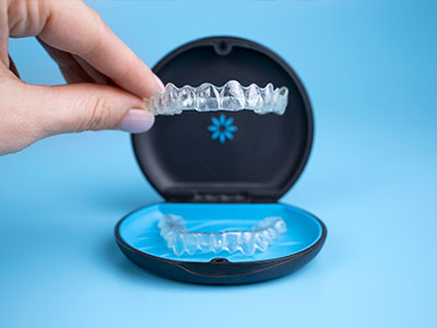 A hand holding a clear plastic tray with a blue mouth guard, showcasing its design and features.