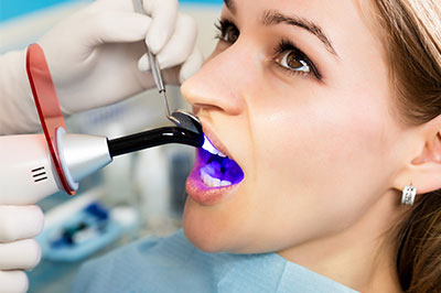 The image shows a person seated in a dental chair, wearing a protective gown and cap, with their mouth open wide to accommodate a dental device that appears to be a scanner or sensor.