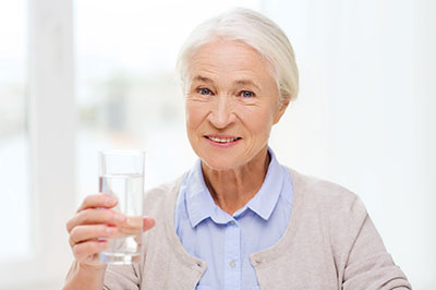 An elderly woman is holding a glass of water to her mouth.