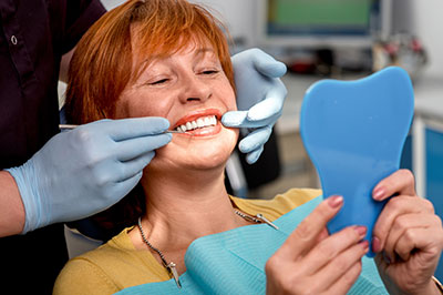 A woman in a dental chair receiving a teeth cleaning, with a dental hygienist wearing blue gloves and using dental instruments.