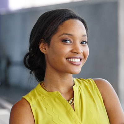 A young woman with a radiant smile, wearing a yellow top and posing for the photo.