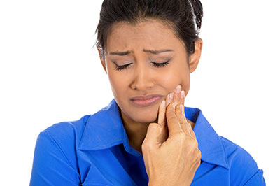 A woman in a blue shirt, with her mouth open, examines her teeth.