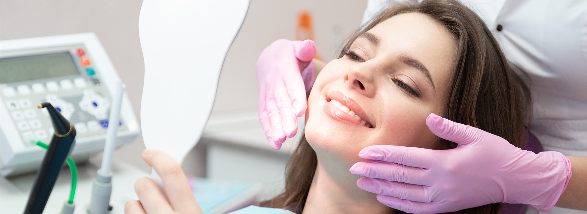 A woman sitting in a dental chair with a dentist performing a procedure on her teeth.