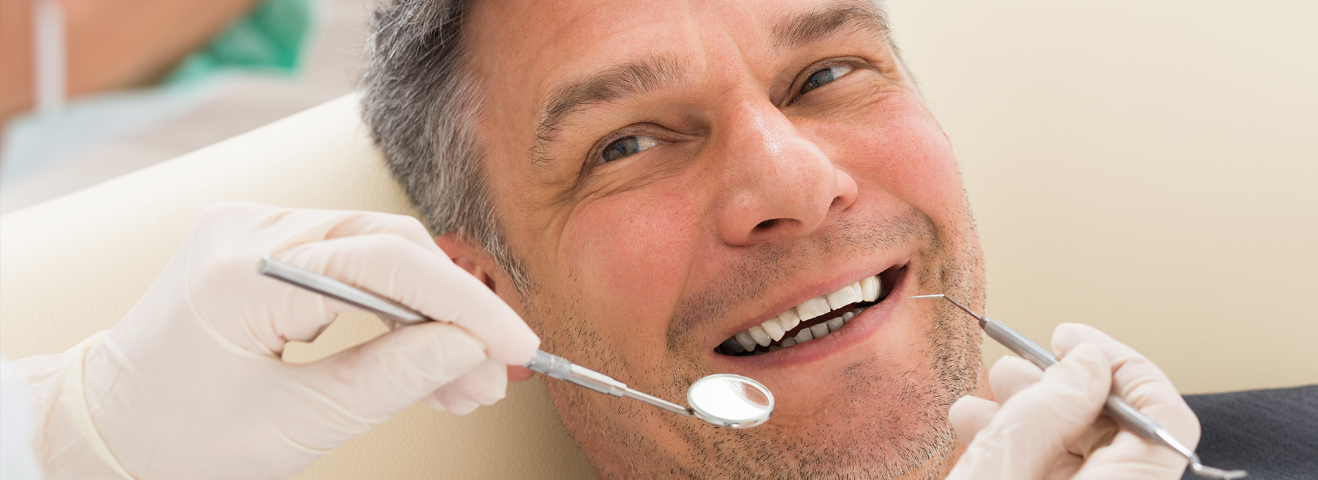 A smiling man in a dental chair, receiving dental treatment with a dentist working on him.