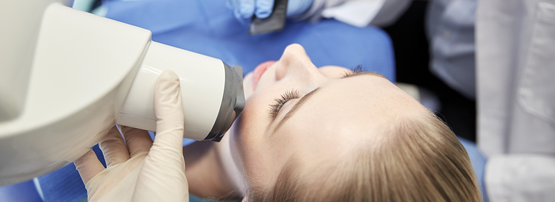 A person receiving a medical procedure, with a device attached to their face and a healthcare professional performing the procedure.