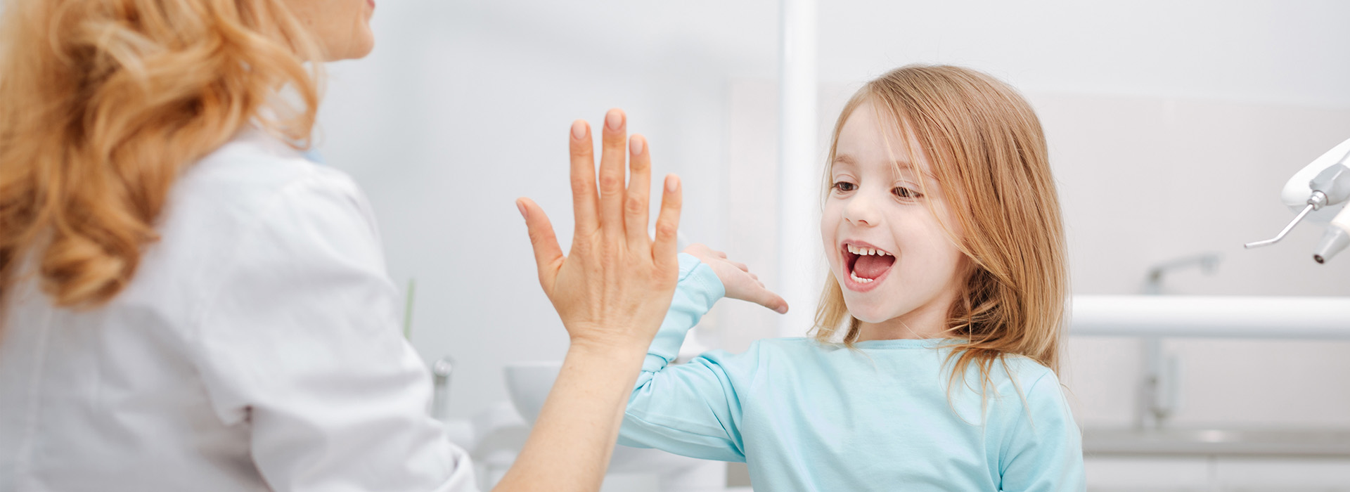 An image of a woman and a child in what appears to be a dental setting, with the woman gesturing towards the child.