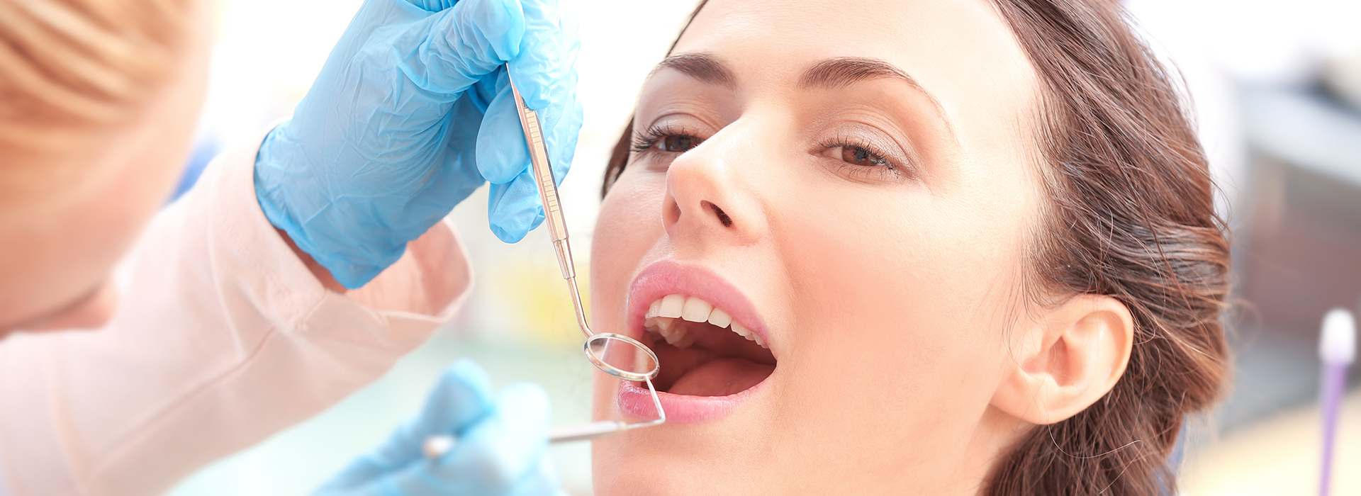 The image shows a person receiving dental care, with a dentist working on their teeth and a dental hygienist assisting.