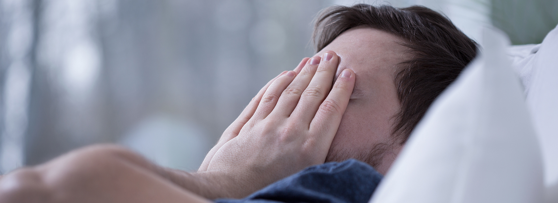 A person lying in bed, with their face partially obscured by a hand.