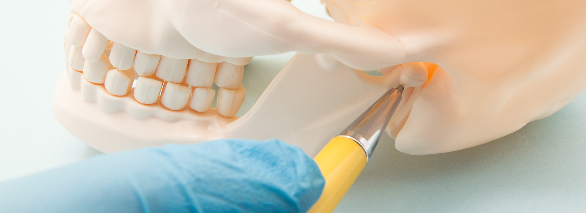 A close-up of a dental procedure with a focus on the dentist s hand holding a yellow instrument and a tooth model.