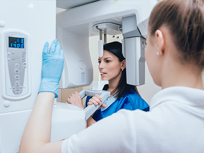 A woman in a blue lab coat is standing next to a large, modern 3D scanner, with another person observing the equipment.