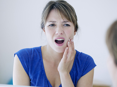 The image shows a woman with her mouth open and hand on her chin, expressing surprise or concern, while looking at her reflection in the mirror.