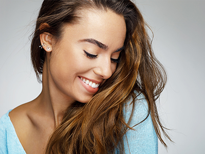 A smiling woman with long hair, wearing a light blue top, against a plain background.