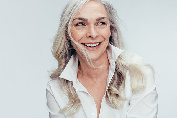 The image is a portrait of an adult woman with blonde hair and a white shirt, smiling slightly and looking directly at the camera.