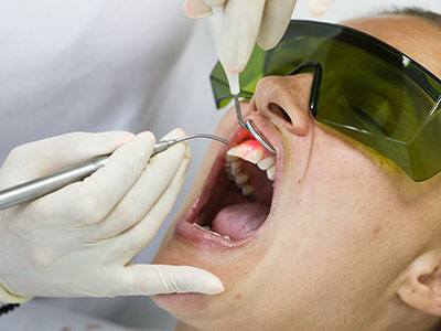 A person receiving dental treatment with a dentist performing the procedure, visible through a mirror.