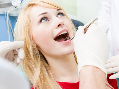 A woman in a red shirt sitting in a dental chair, receiving dental treatment from a professional.