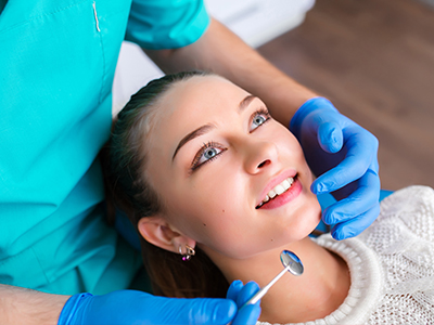 A woman receiving dental care, with a dental professional adjusting her teeth using dental tools.