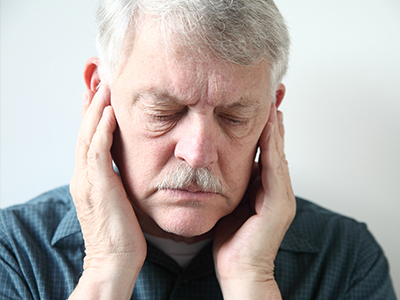 An elderly man with a mustache is seen holding his hand to his ear, appearing to be in deep thought or possibly experiencing discomfort.